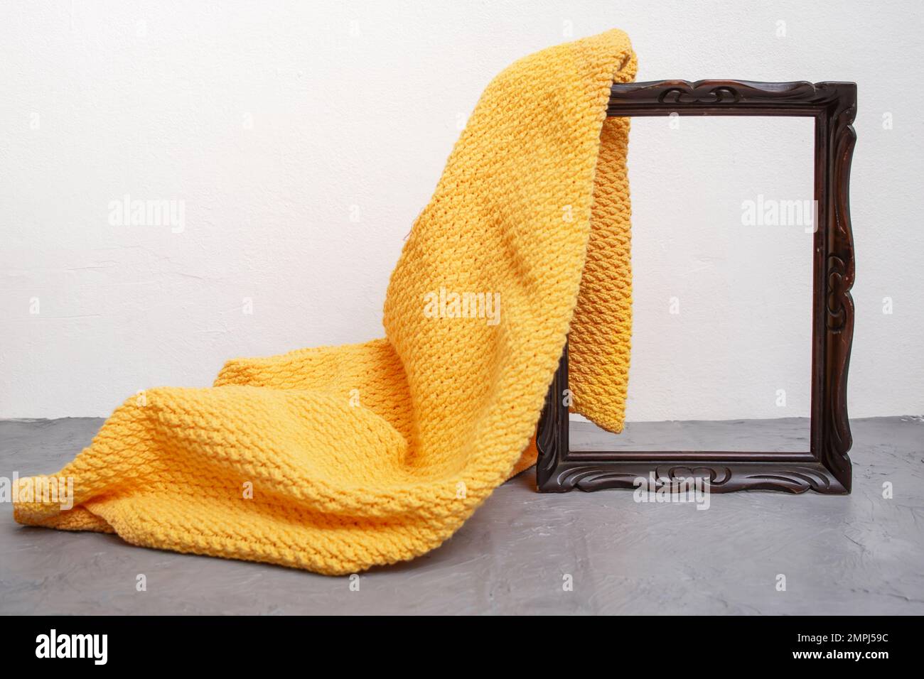 Orange crochet blanket unveiling a wooden frame on a gray cement countertop, product presentation display template Stock Photo