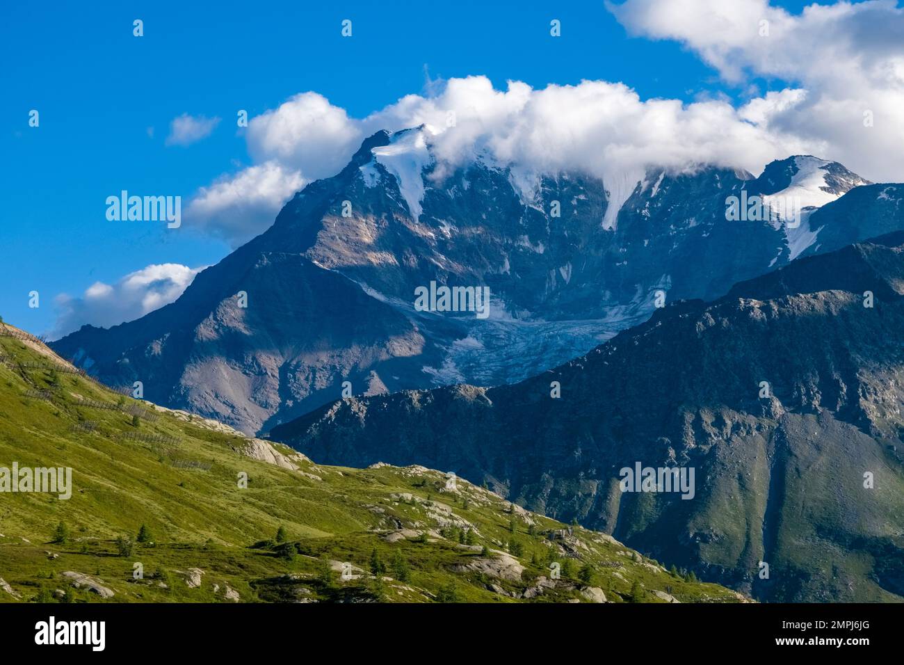 The summits of the mountains Fletschhorn, Senggchuppa and Schilthorn, partly covered in clouds, rising over Simplon Pass. Stock Photo