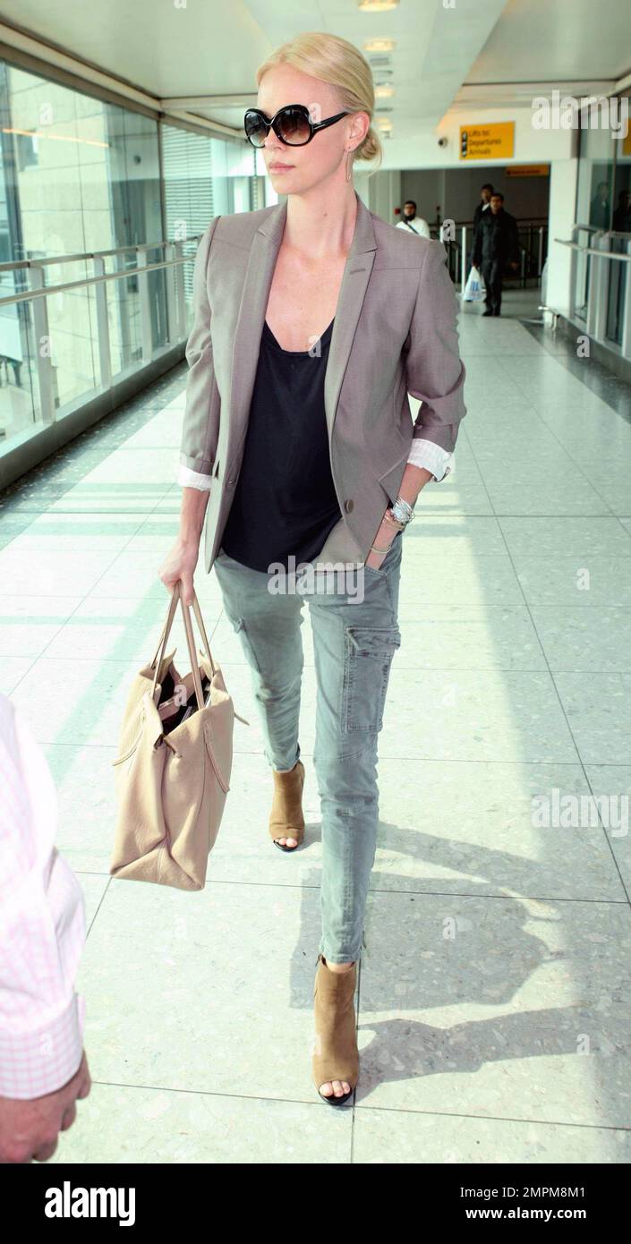 Looking casual, but chic, actress Charlize Theron wears a brown jacket over  a black top, green pants and brown heels as she arrives at London Heathrow  after a long-haul flight from Los