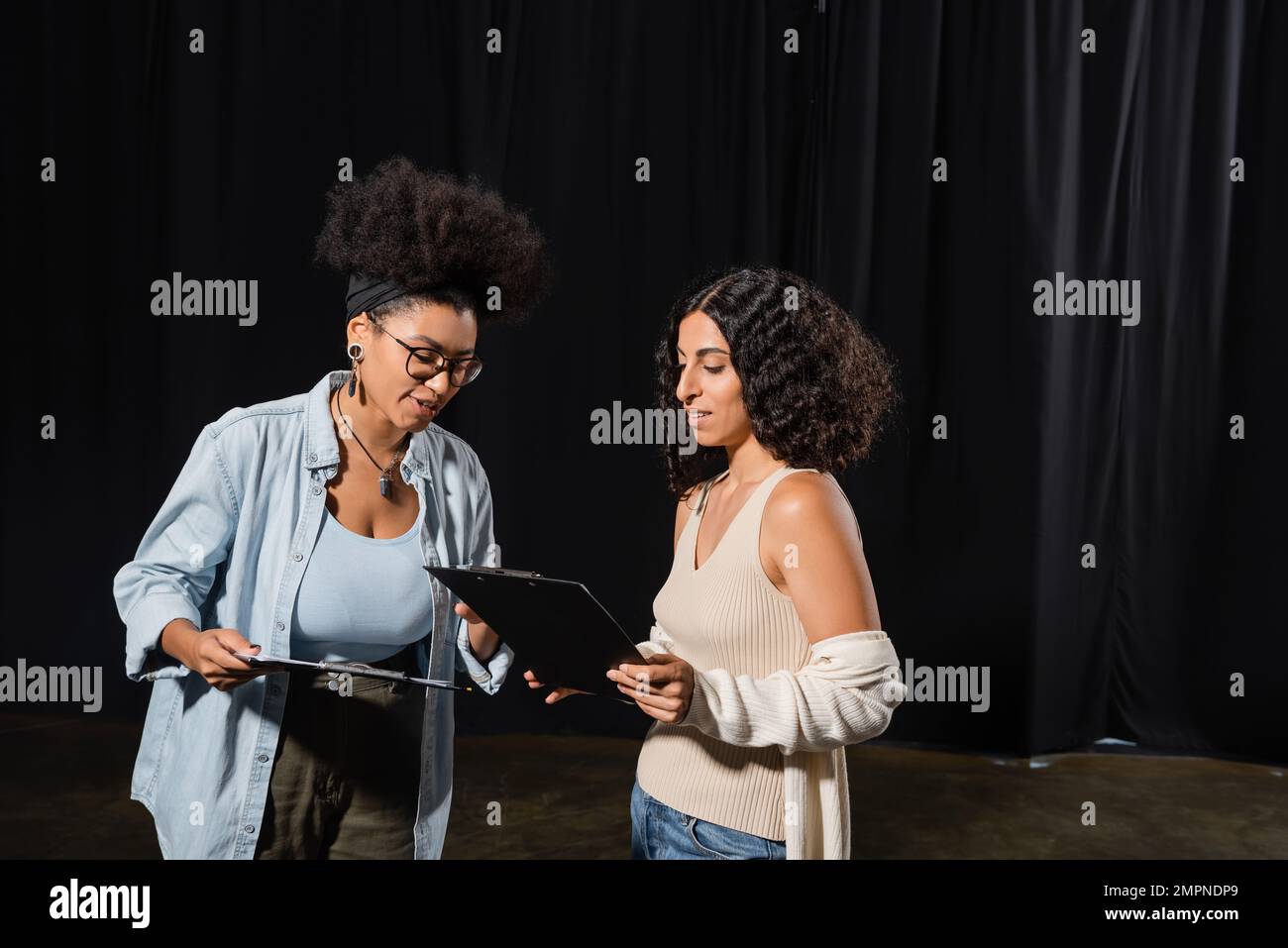 young interracial actresses looking at clipboards with scenarios in