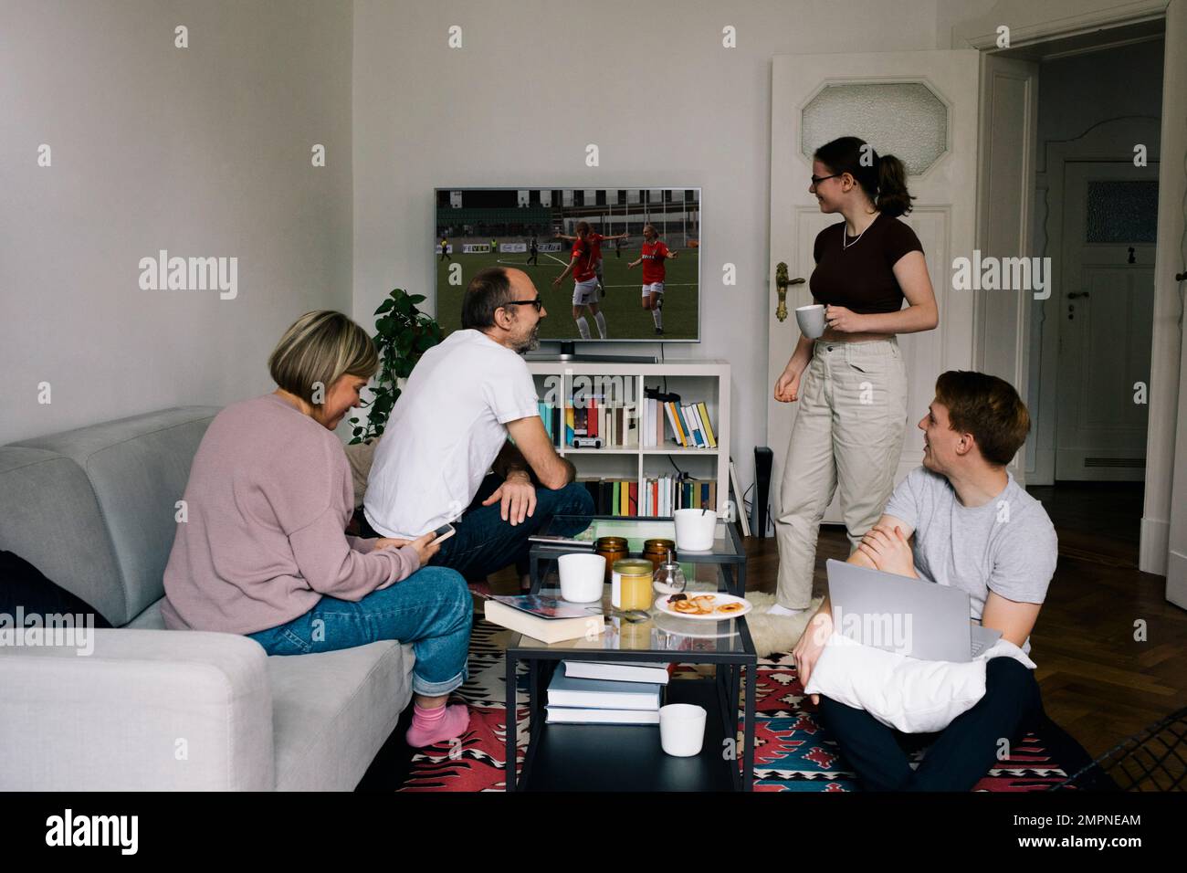 Family talking to daughter while watching football on TV in living room at home Stock Photo