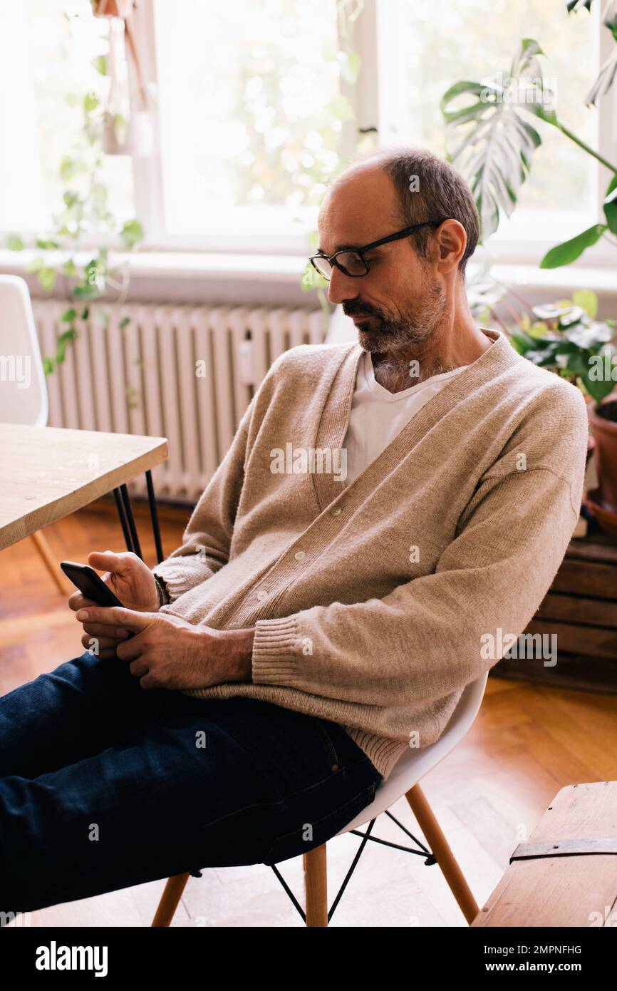 Man using smart phone while sitting on chair at home Stock Photo