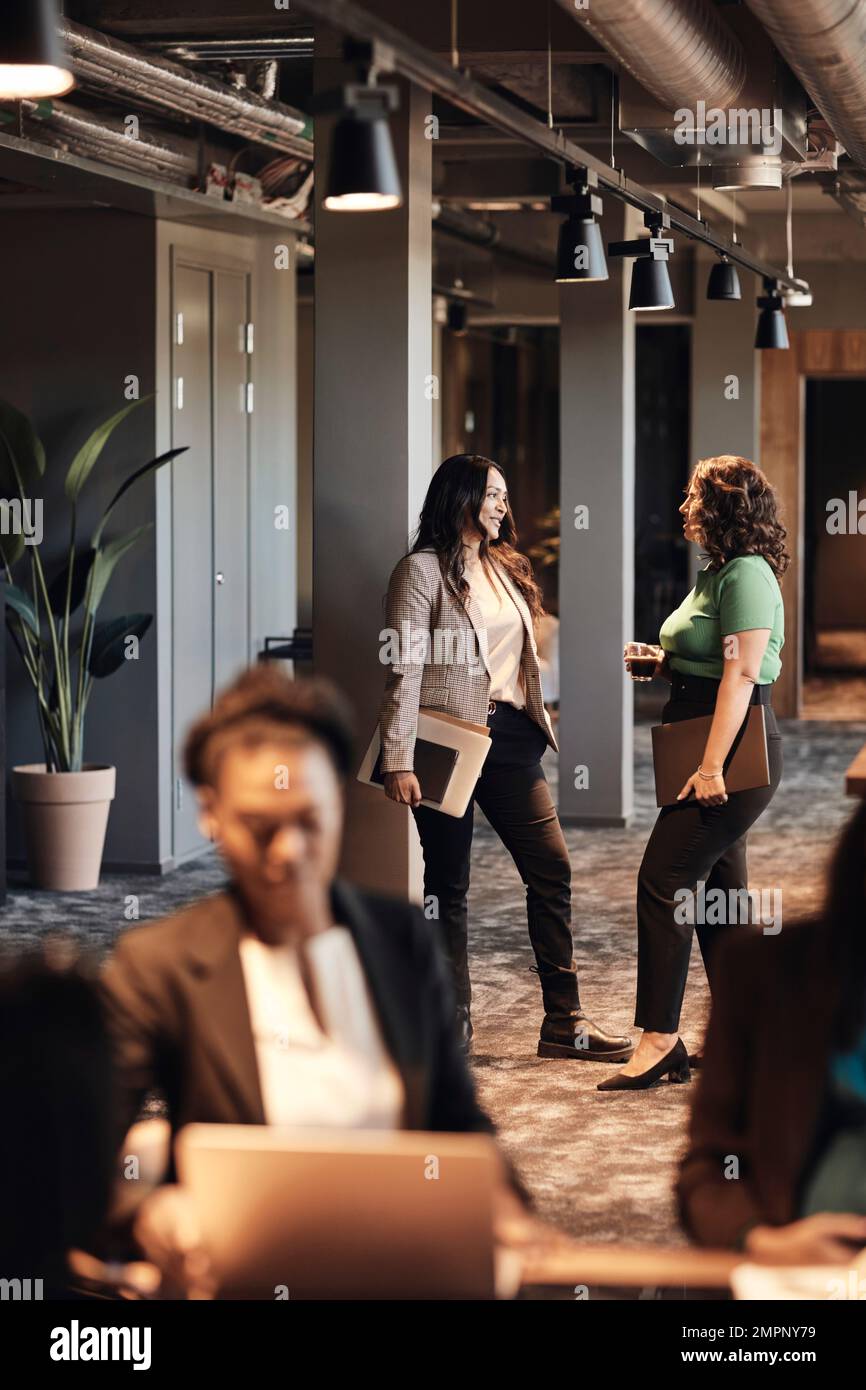 Multiracial business colleagues talking to each other while standing in office Stock Photo