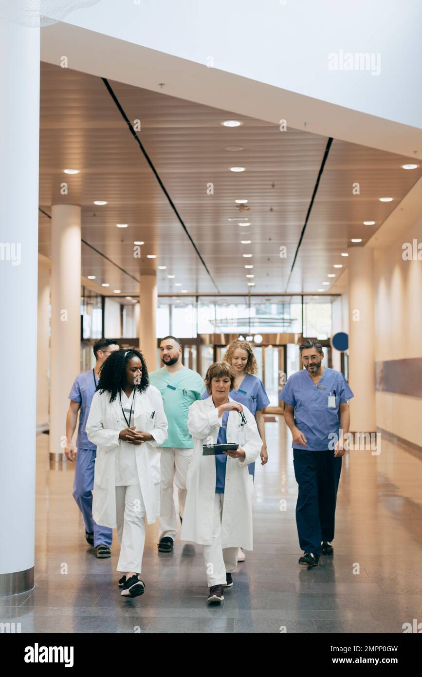 Male and female healthcare workers discussing while walking in hospital Stock Photo