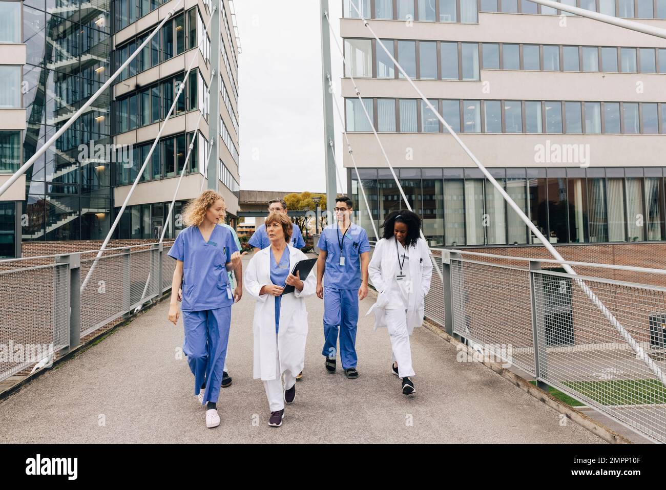 Multiracial healthcare workers discussing while walking on bridge by hospital building Stock Photo