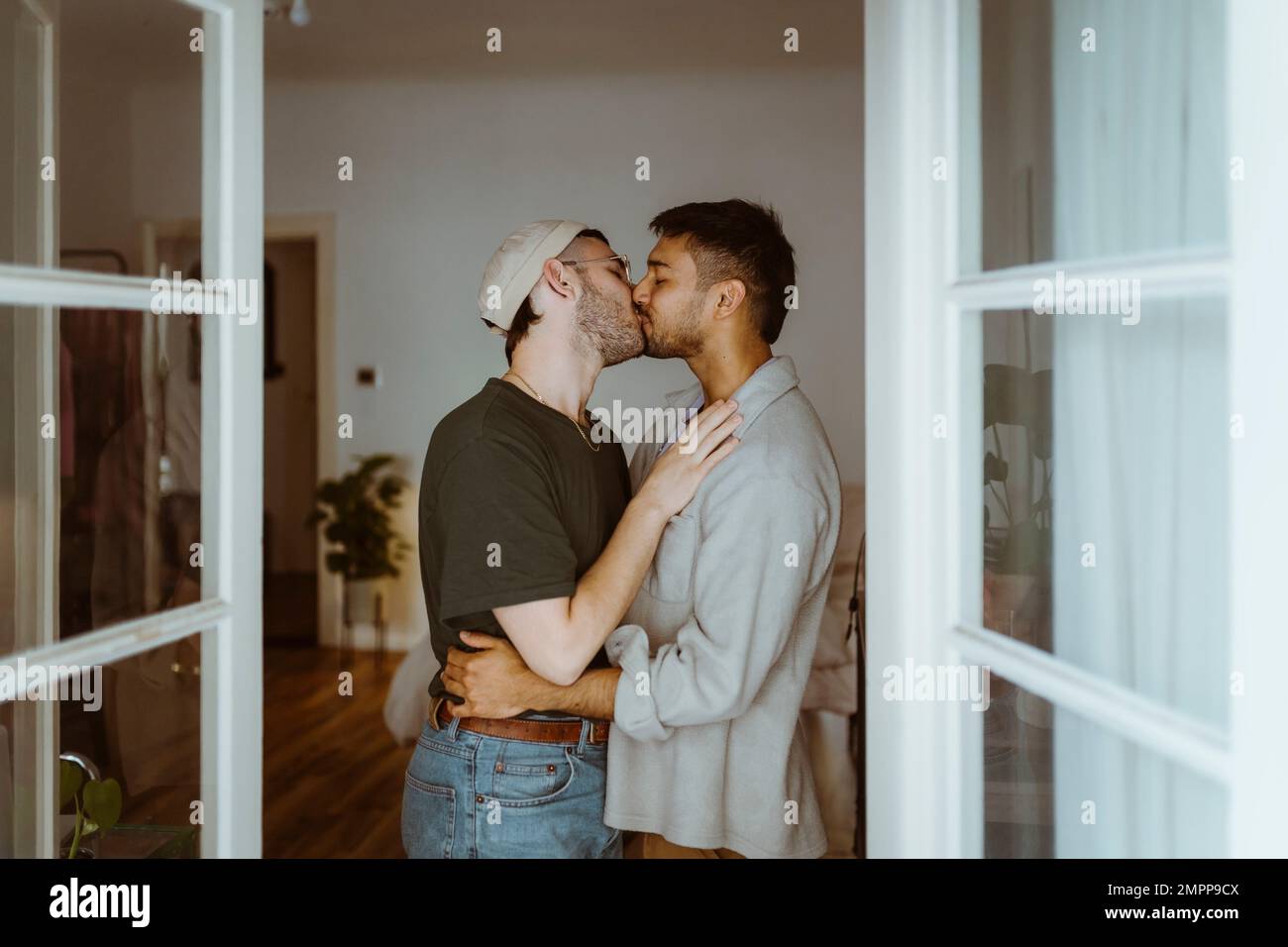 Side view of romantic gay couple kissing each other seen through doorway Stock Photo