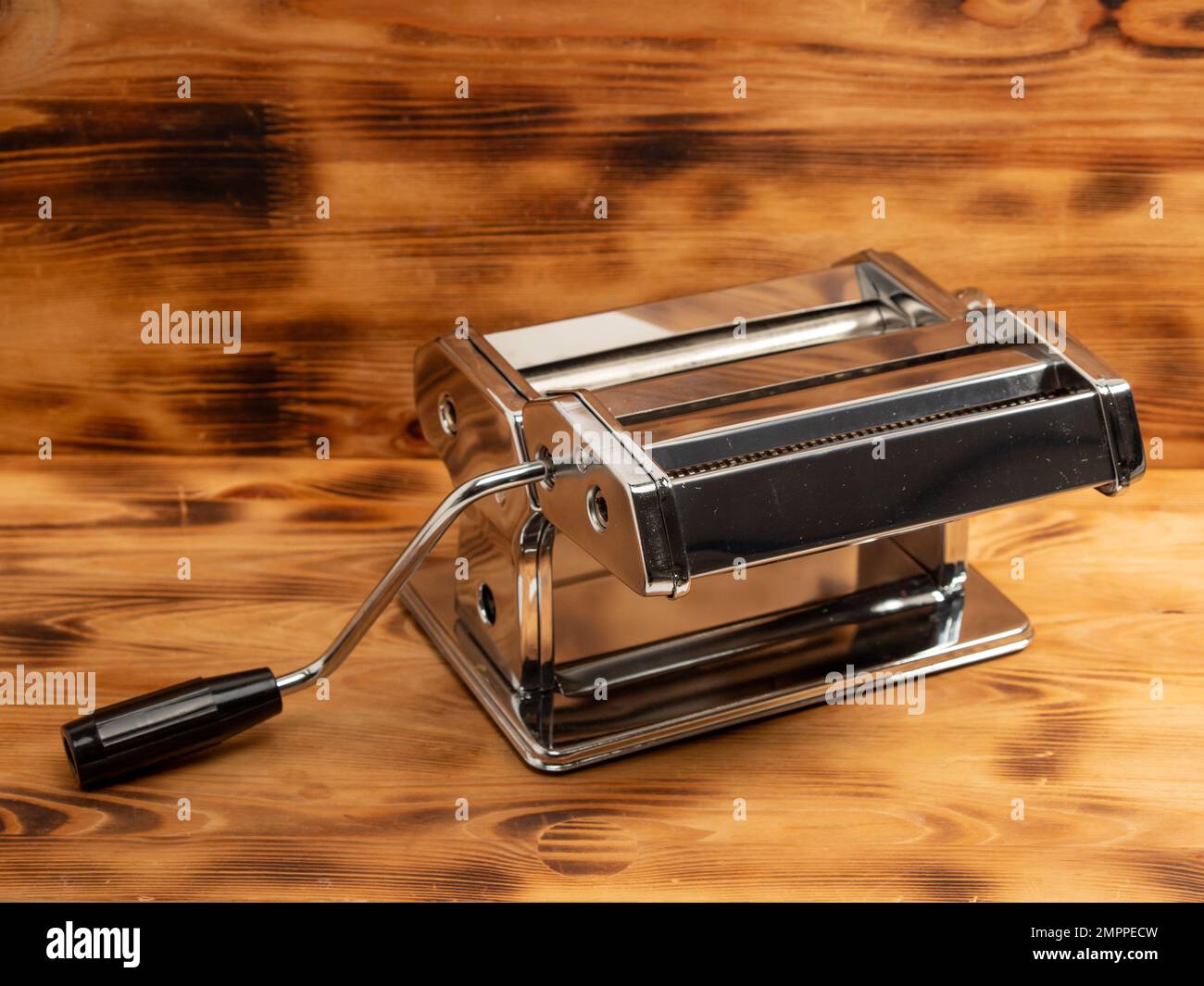 https://c8.alamy.com/comp/2MPPECW/manual-machine-for-rolling-dough-and-pasta-noodle-cutter-chrome-plated-steel-anodized-aluminium-wooden-background-2MPPECW.jpg