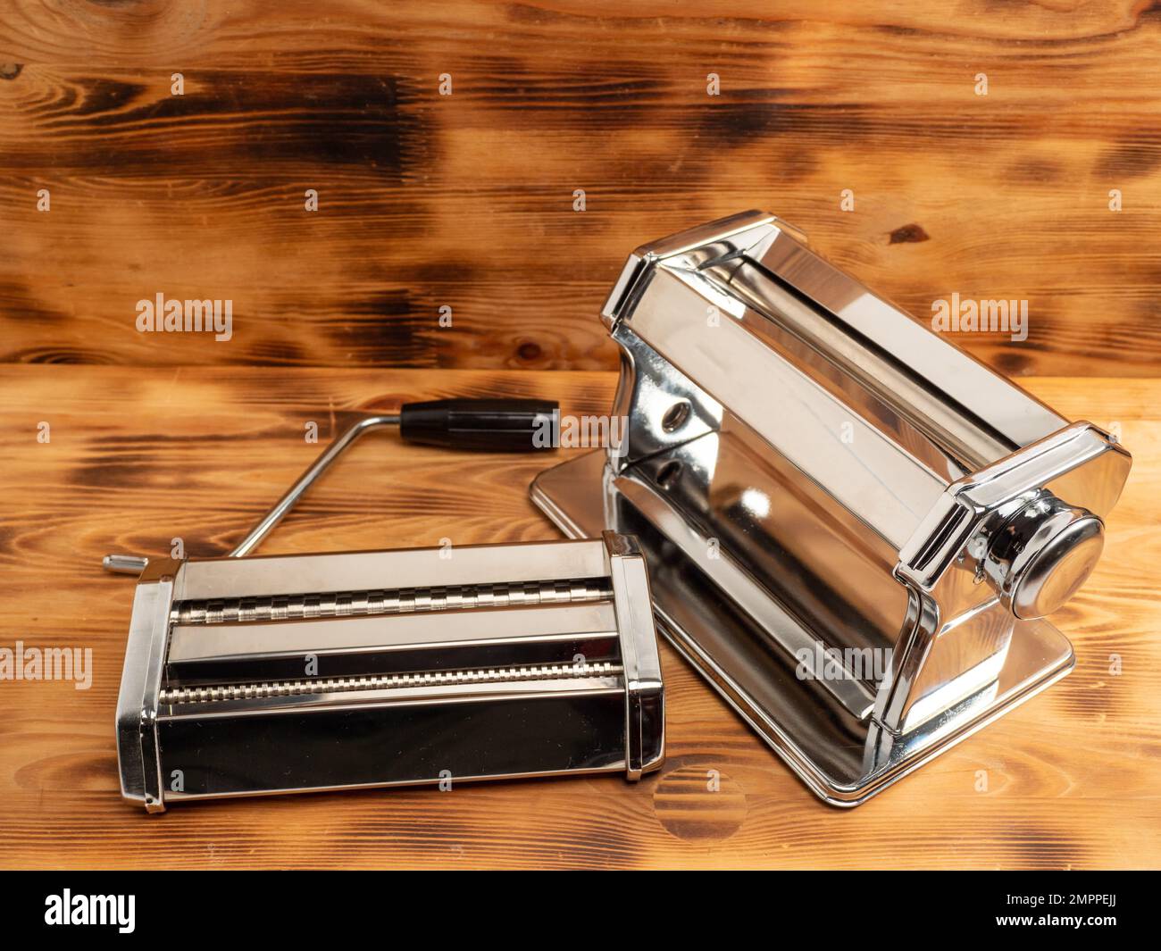 https://c8.alamy.com/comp/2MPPEJJ/manual-machine-for-rolling-dough-and-pasta-noodle-cutter-chrome-plated-steel-anodized-aluminium-wooden-background-2MPPEJJ.jpg