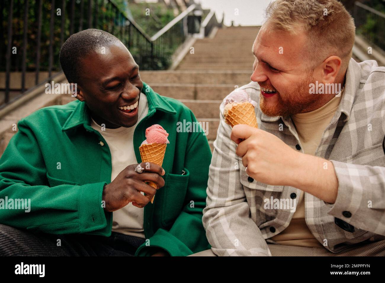 Happy multiracial male friends enjoying ice creams while sitting on steps Stock Photo