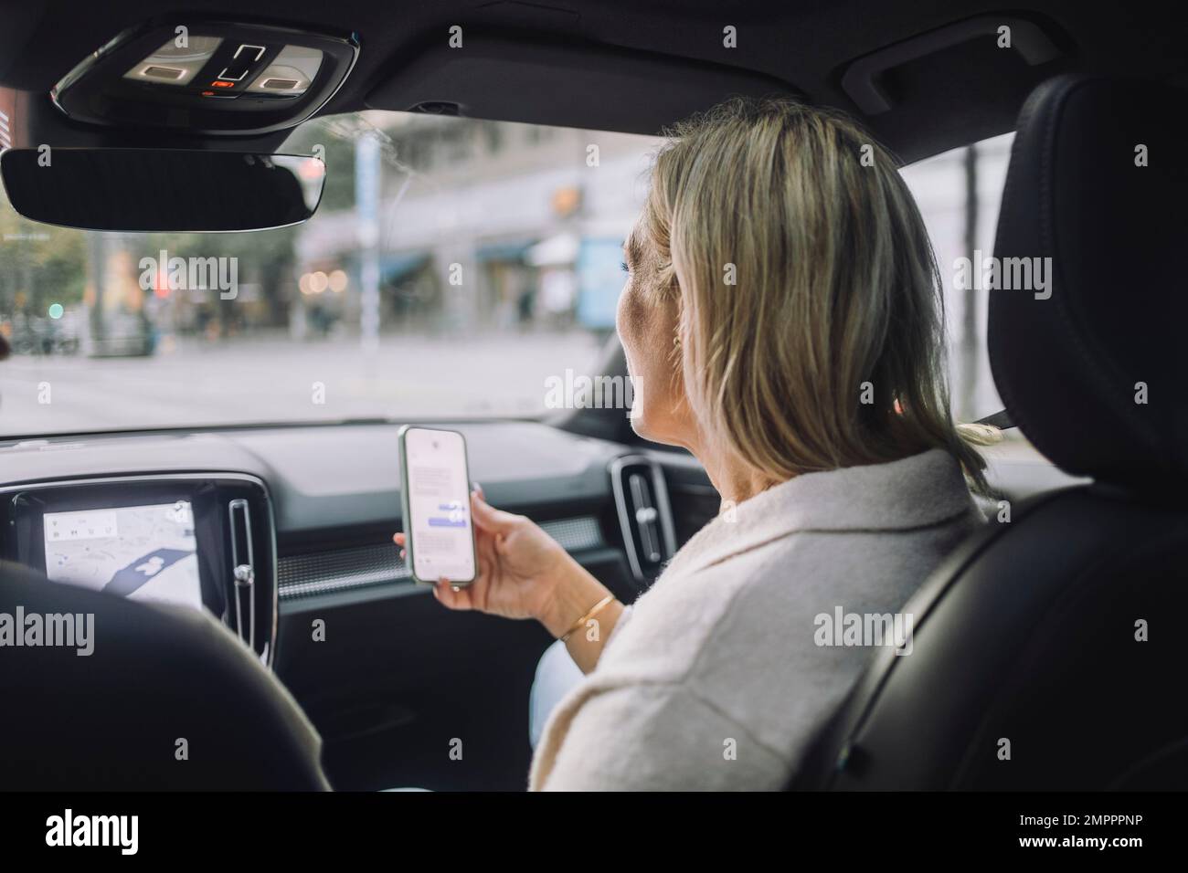Mature woman using smart phone while sitting in front passenger seat Stock Photo