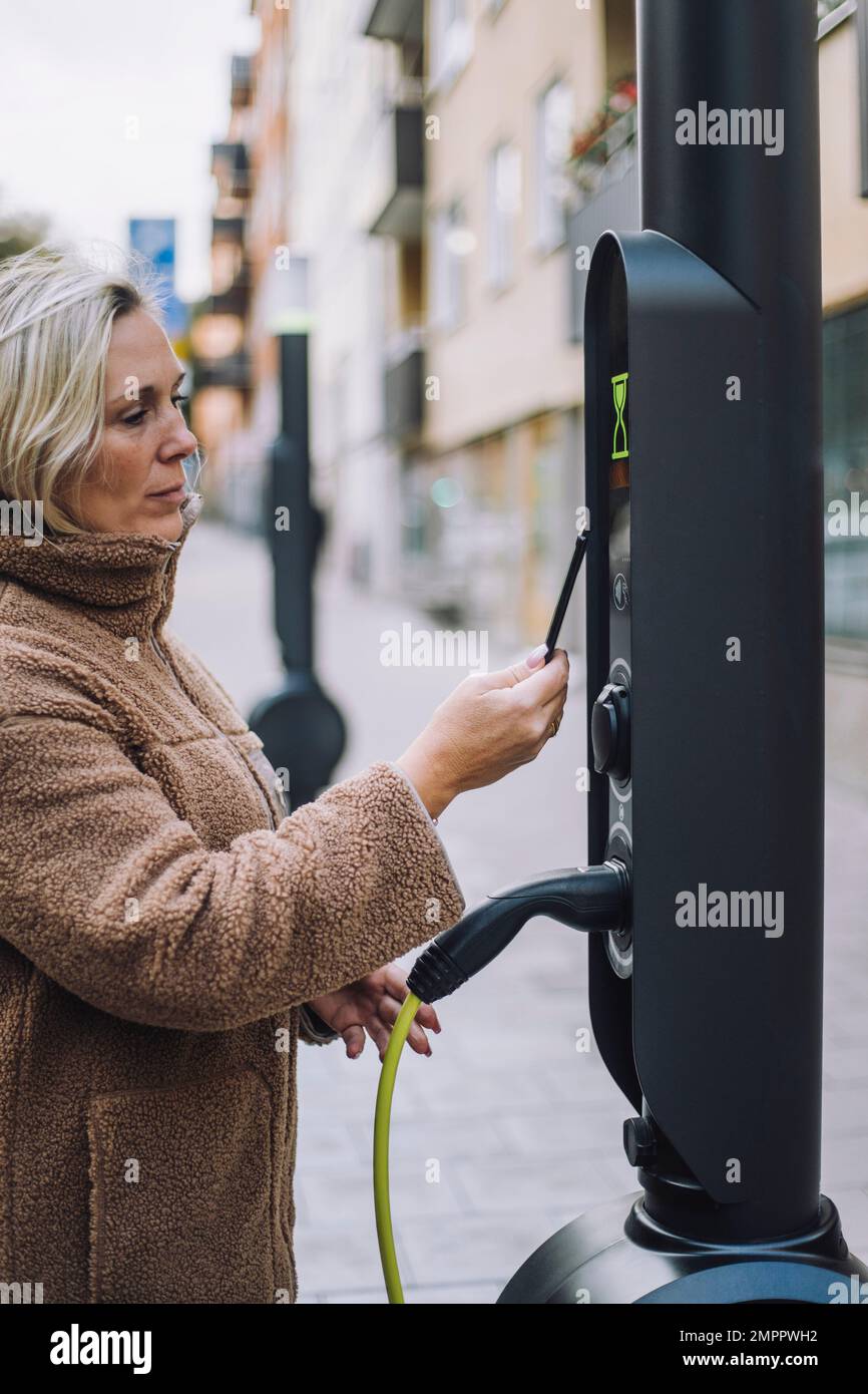 Mature woman paying via digital wallet at electric vehicle charging station Stock Photo