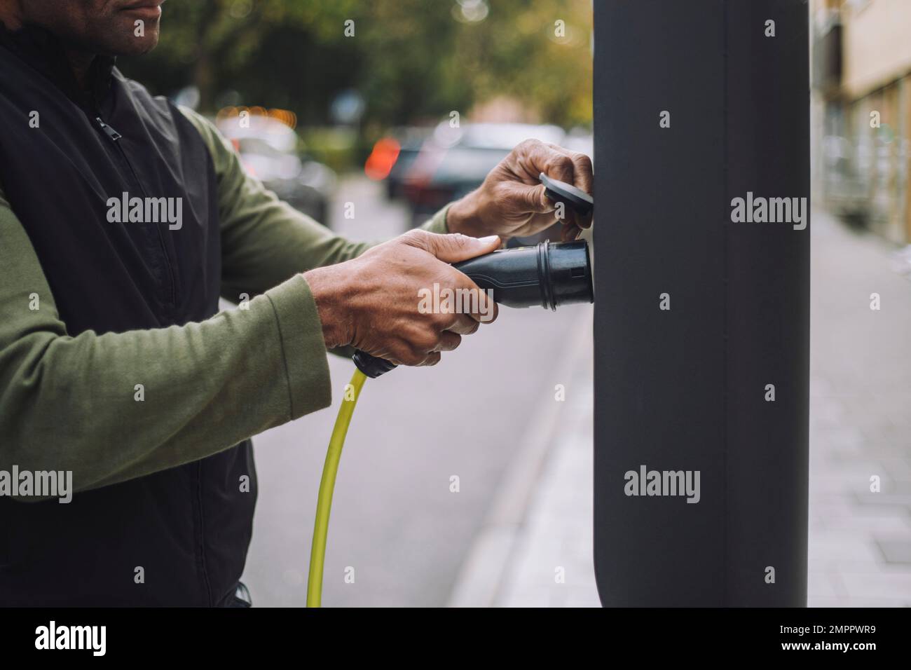 Man removing charger plug from kiosk at car charging station Stock