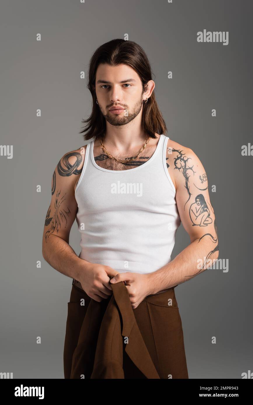 Tattooed long haired man holding jacket standing isolated on grey Stock Photo