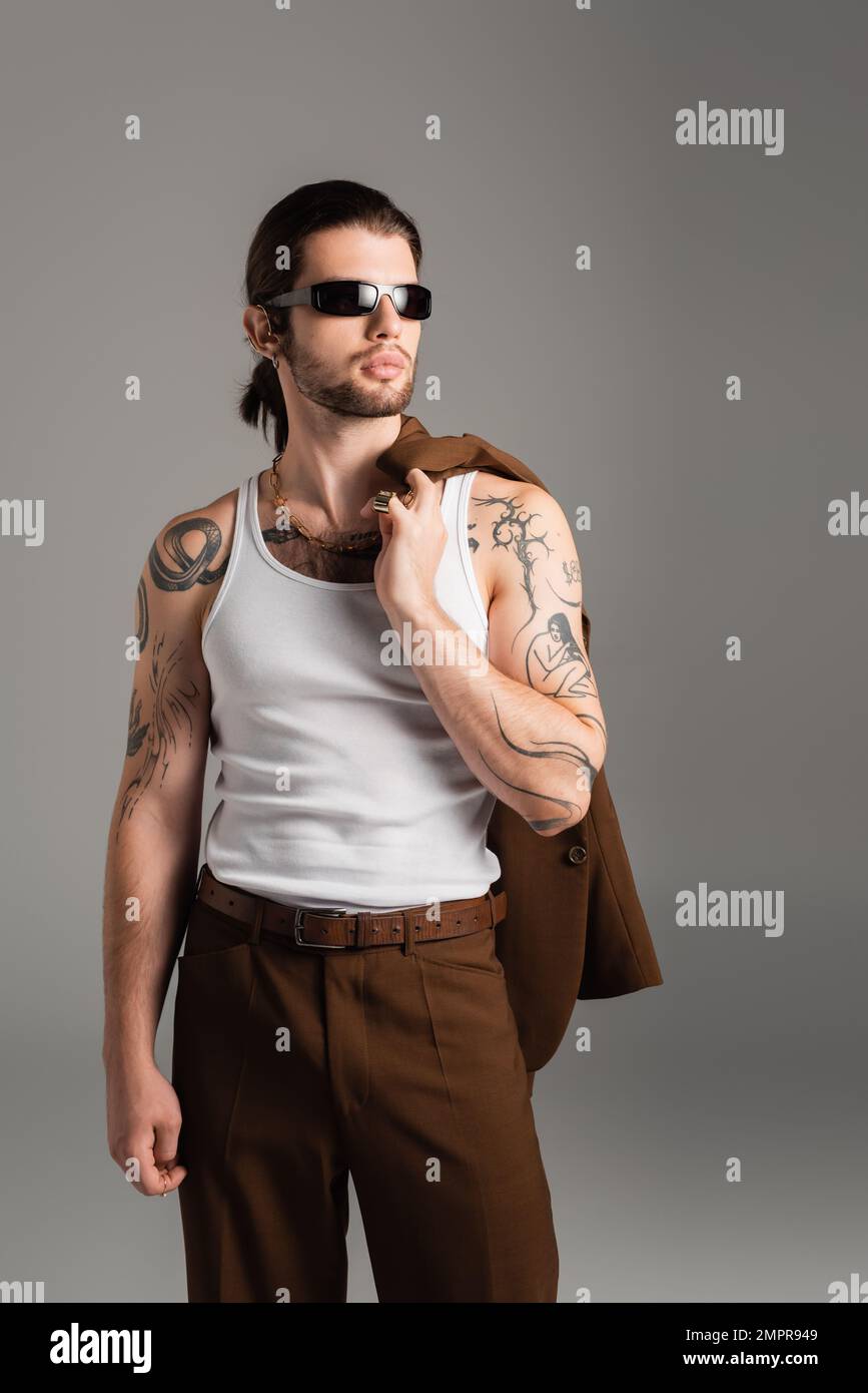 Tattooed man in sunglasses holding jacket isolated on grey Stock Photo