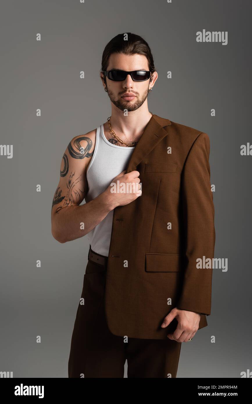 Bearded tattooed man in sunglasses holding jacket isolated on grey Stock Photo