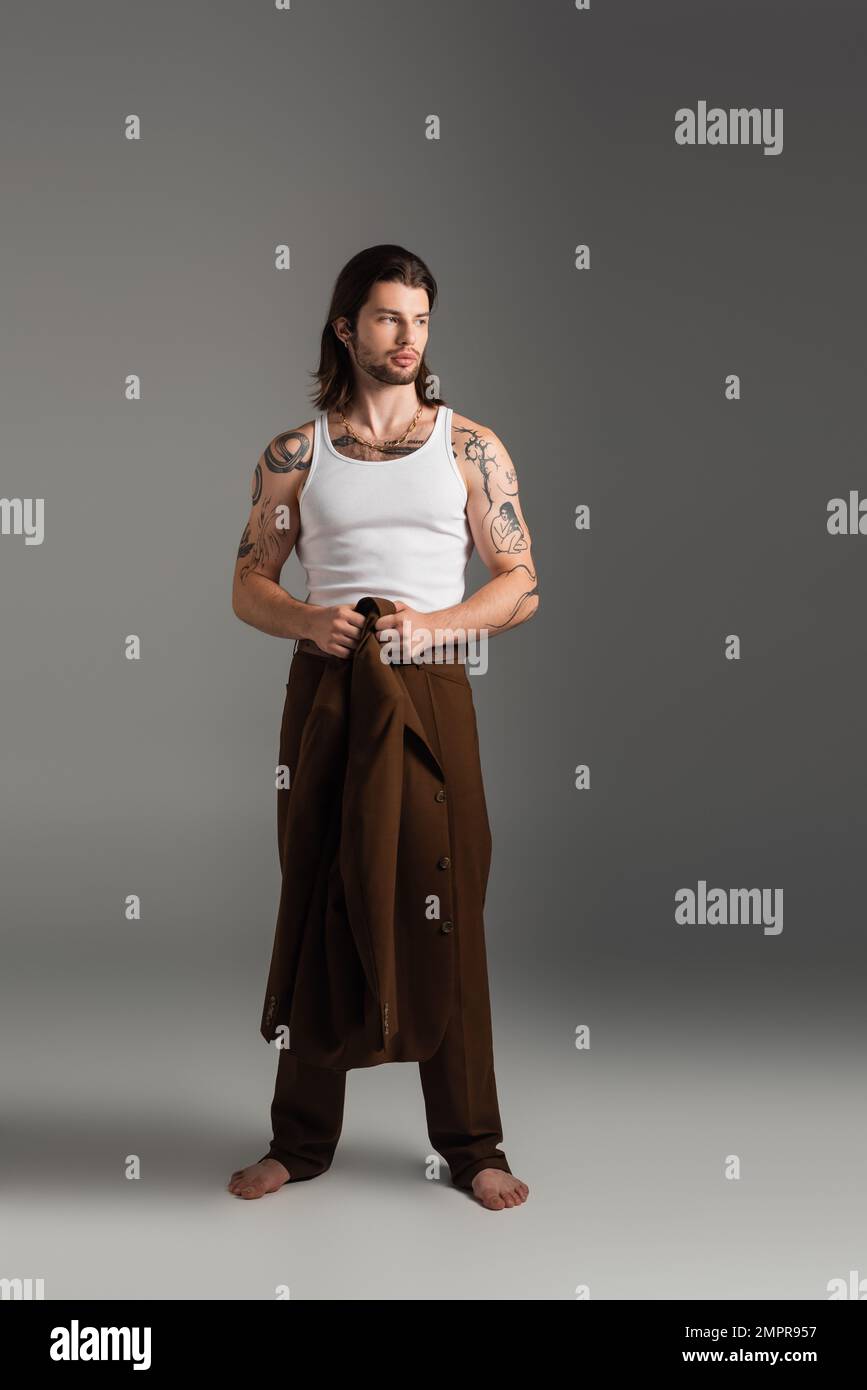 Full length of barefoot and tattooed model holding jacket on grey background Stock Photo