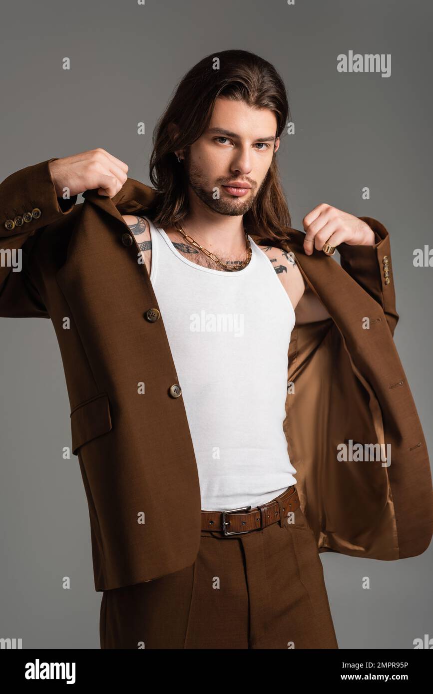 Trendy long haired man with tattoo wearing jacket isolated on grey Stock Photo