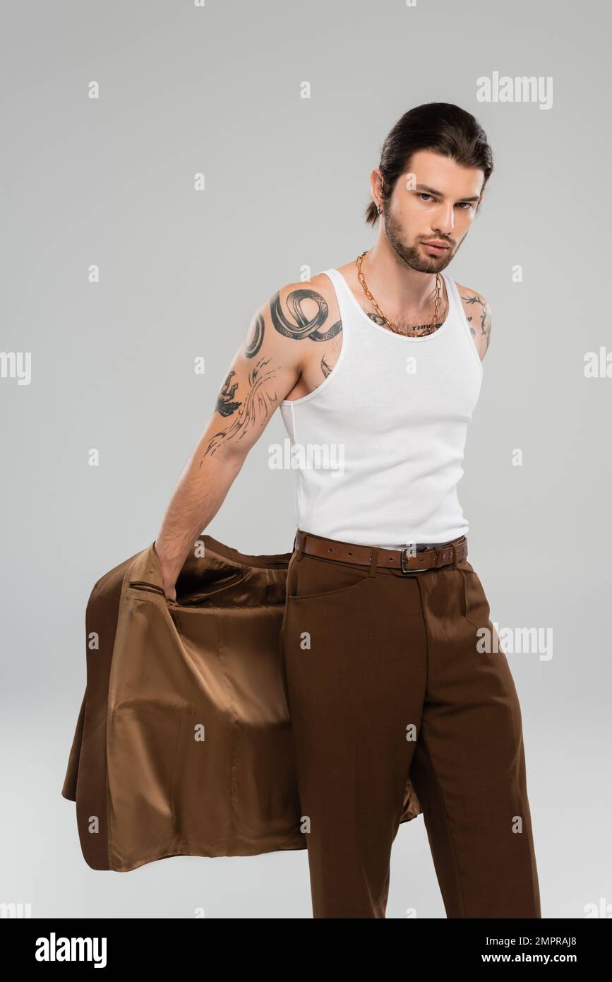 Tattooed man in sleeveless shirt holding jacket isolated on grey Stock Photo