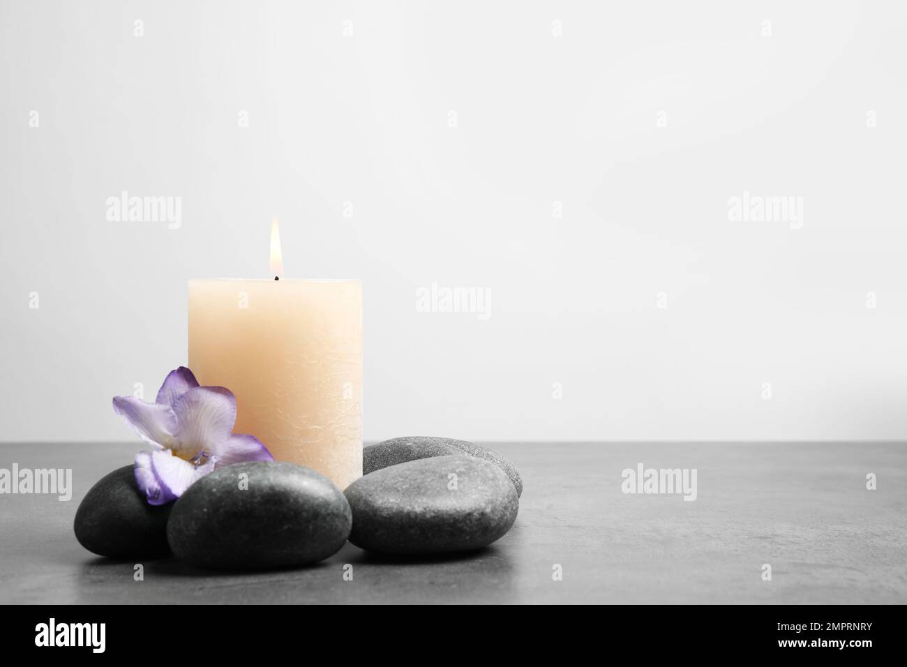 Spa stones, burning candle and freesia flower on grey table, space for ...