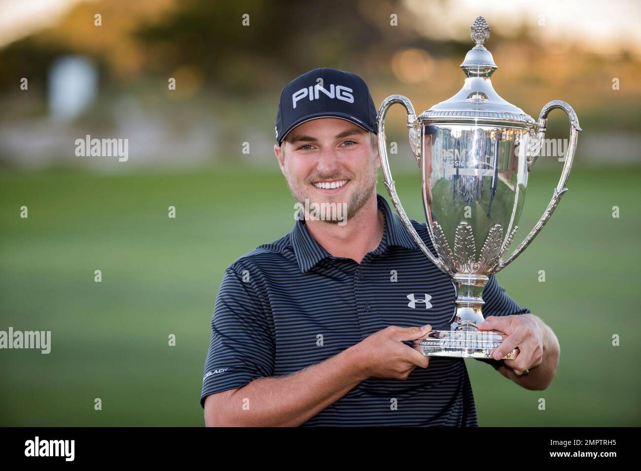 Austin Cook holds the trophy on the 18th green after winning the final round of the RSM Classic golf tournament on Sunday, Nov. 19, 2017, in St