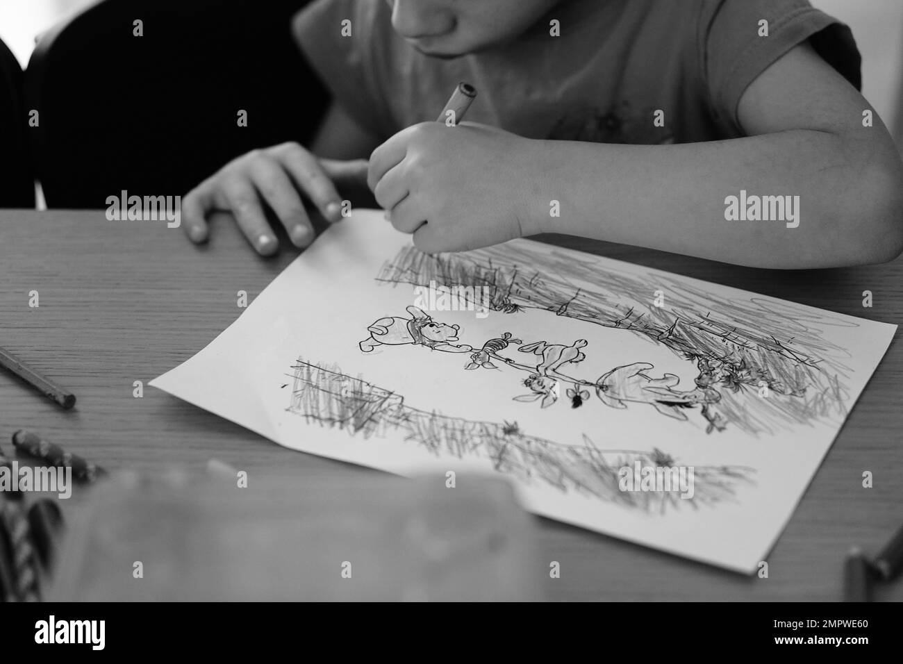 A caucasian boy sitting by a table and coloring Winnie The Pooh pages Stock Photo