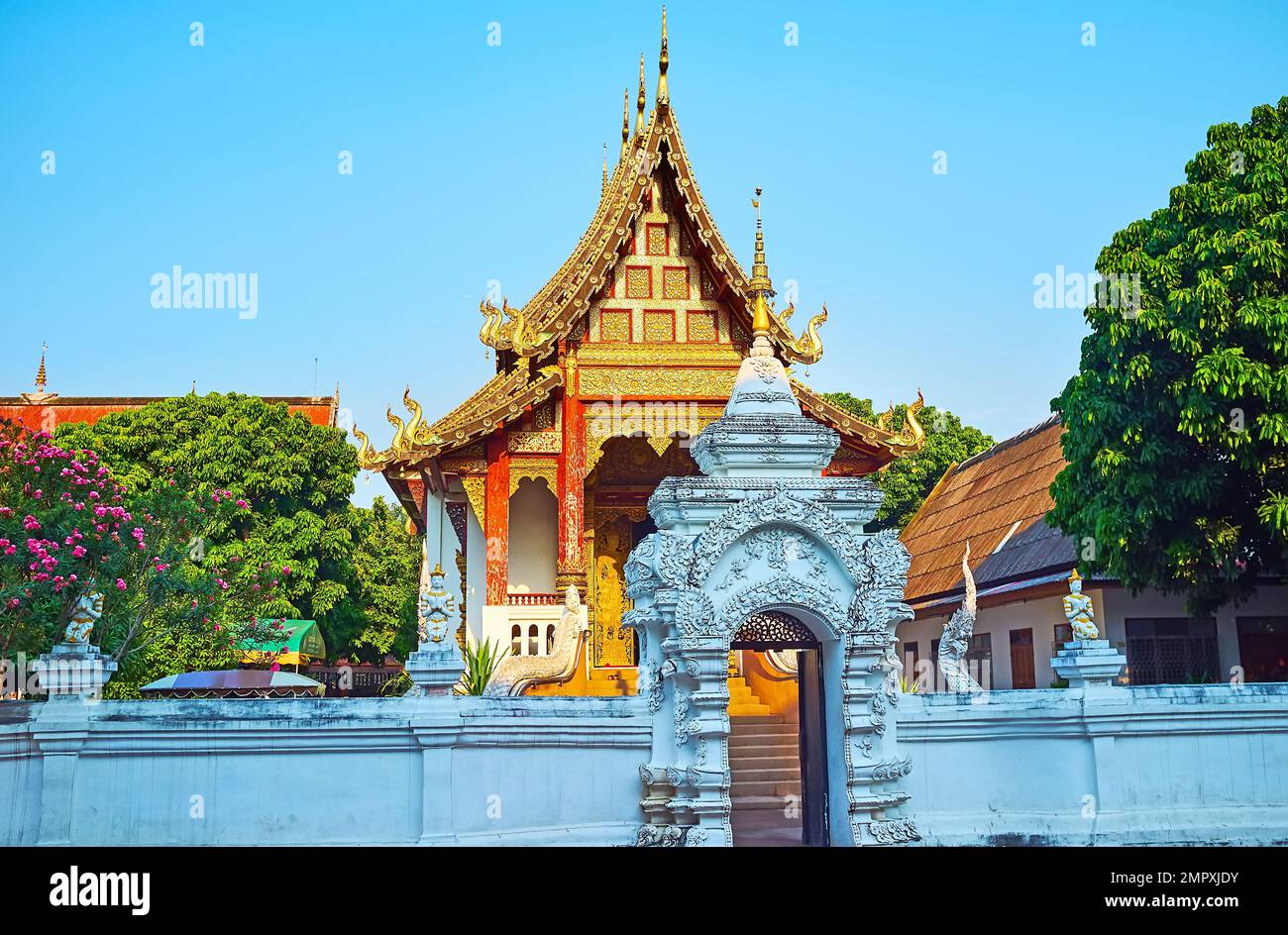 The carved white gate of Wat Chang Taem temple, decorated with reliefs, golden hti umbrella, devata sculptures on the fence, Chiang Mai, Thailand Stock Photo