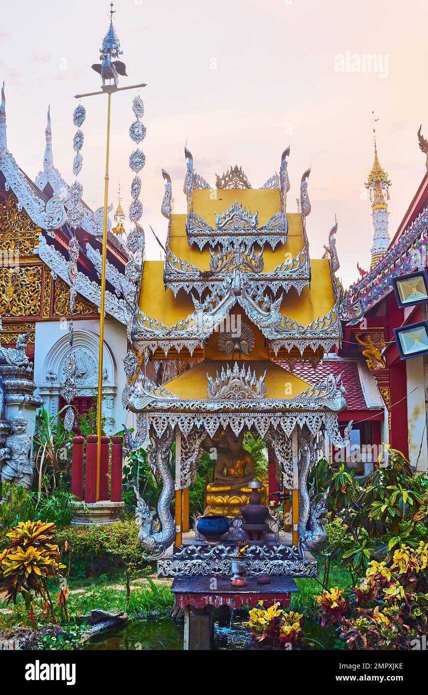 The tiny shrine with ornate pyathat roof and Buddha image in garden of Wat Mahawan, Chiang Mai, Thailand Stock Photo
