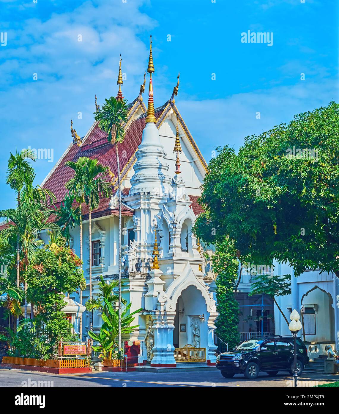 The elegant white monastic building of Wat Saen Muang Ma temple with gilt hti umbrellas and green palms around it, Chiang Mai, Thailand Stock Photo