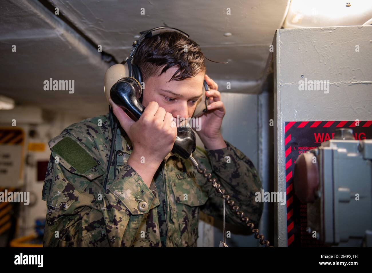 221121-N-IW069-1001 SAN DIEGO (Nov. 21, 2022) Aviation Ordnancemen Airman Logan Dickinson, a native of Longview, Wash., works as a phone talker while moving ordnance during a weapons evolution aboard Nimitz-class aircraft carrier USS Carl Vinson (CVN 70). Vinson is currently pierside in its homeport of San Diego. Stock Photo