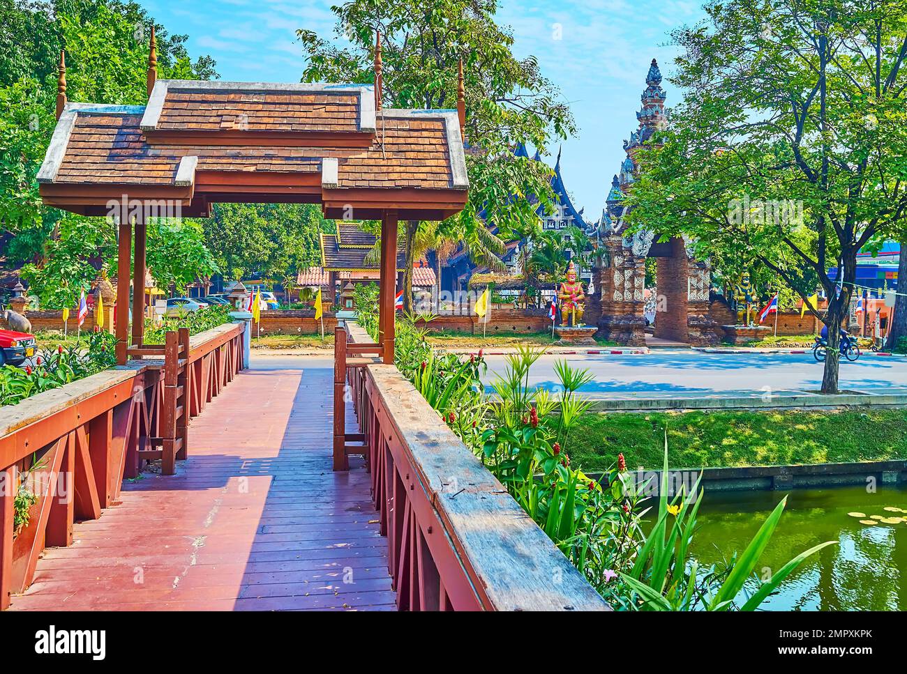 Decorative gate on a footbridge across Old City Moat with a view on shady trees and Wat Lok Moli in the background, Chiang Mai, Thailand Stock Photo