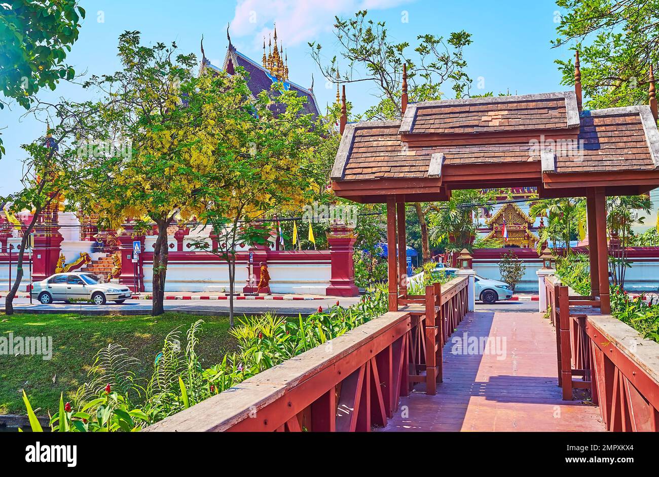 Walk down the wooden footbridge across the Old City Moat, surrounded with lush green park with blooming caragana trees, Chiang Mai, Thailand Stock Photo