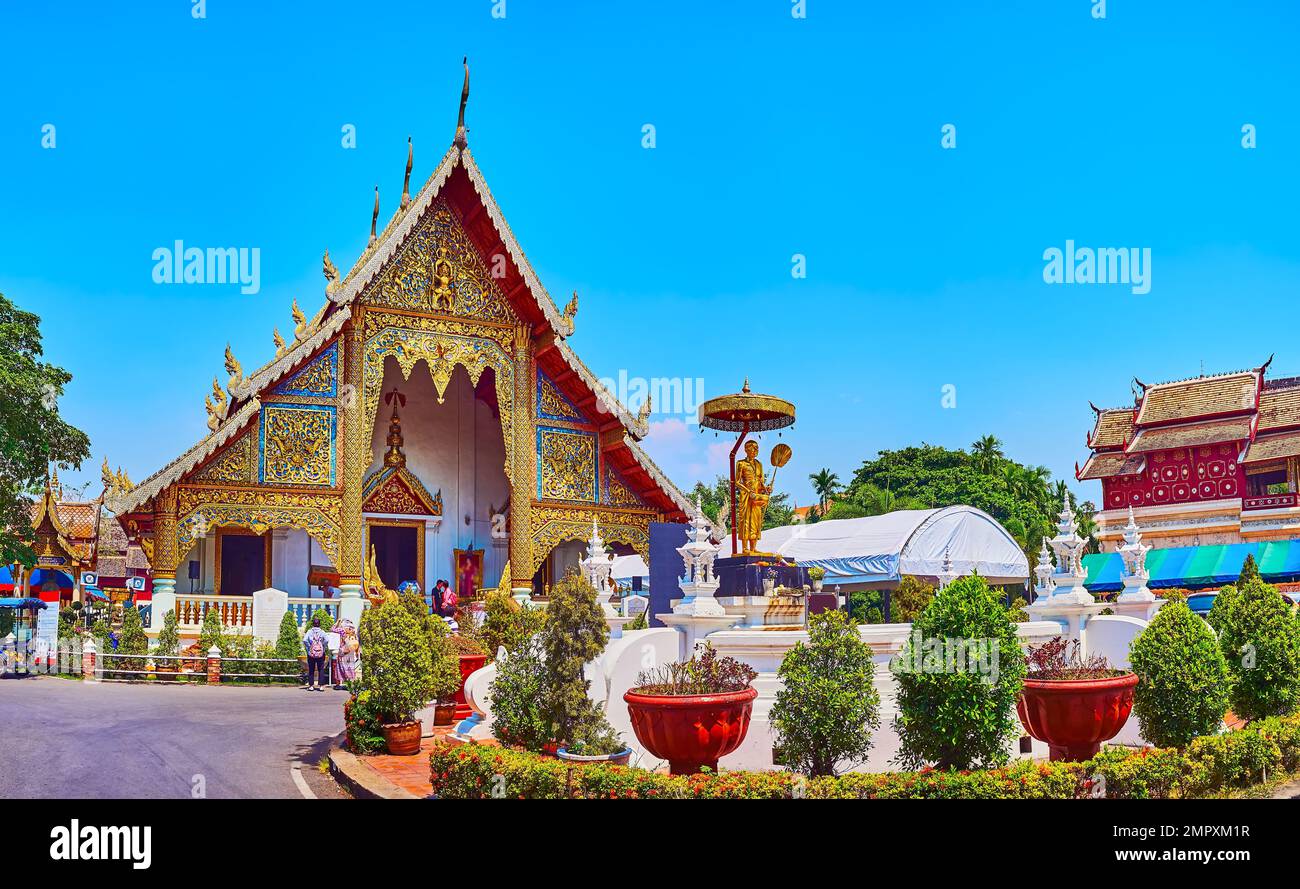 The beautiful flower beds and small thuja trees in pots in front of the carved gilt Viharn Luang of Wat Phra Singh, Chiang Mai, Thailand Stock Photo