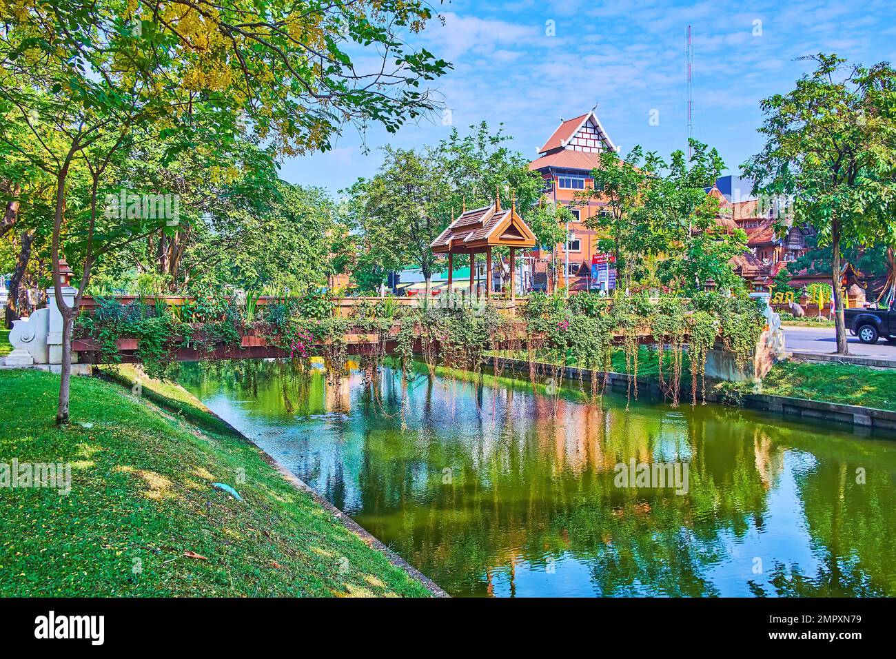 The scenic wooden footbridge across the Old City Moat, decorated with carved gate, hanging green plants and orchids, Chiang Mai, Thailand Stock Photo