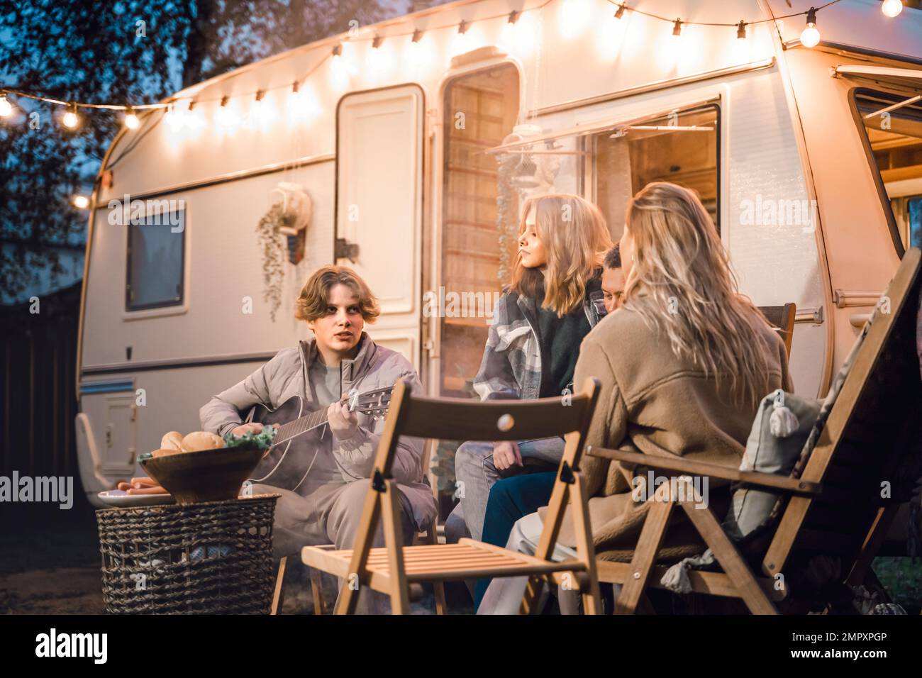 Family trailer travel.Children,brother sister,mom dad playing guitar,singing song at fire.Evening picnic in nature.Holiday barbecue BBQ food.Vacation Stock Photo