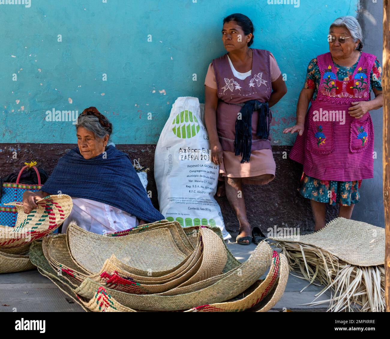 Three indigenous women in traditional dress sell woven palm mats in the market in Ocotlan de