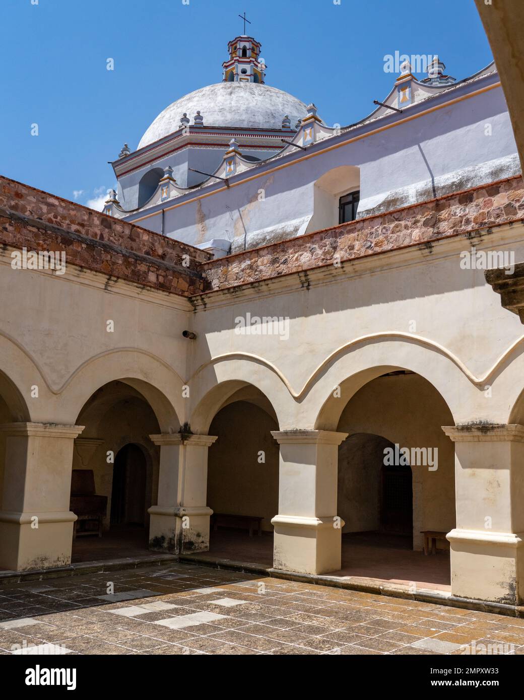 Arches and colonnades of the former monastery of Santo Domingo in Ocotlan de Morelos, Oaxaca, Mexico.  Now a museum.  Behind is the dome of the dome o Stock Photo