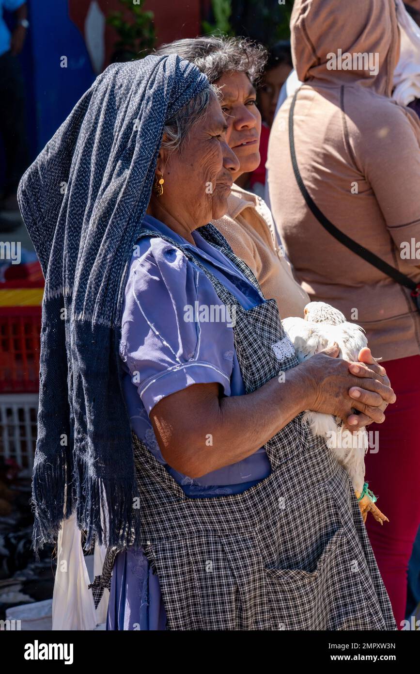An indigenous Zapotec woman in traditional dress selling a chicken in the market in Ocotlan de