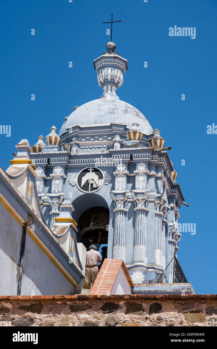 Painted bell tower and bell of the Church of Santo Domingo de Guzman in Ocotlan de Morelos, Oaxaca, Mexico.  A man is standing by the bell. Stock Photo
