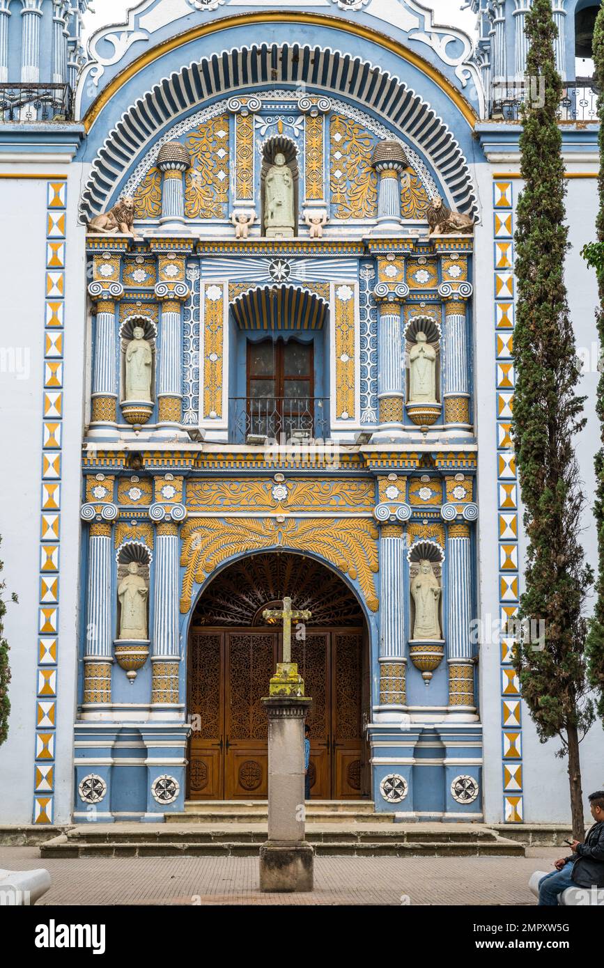 Stone cross in front of the colorful painted facade of the Church of Santo Domingo de Guzman in Ocotlan de Morelos, Oaxaca, Mexico. Stock Photo