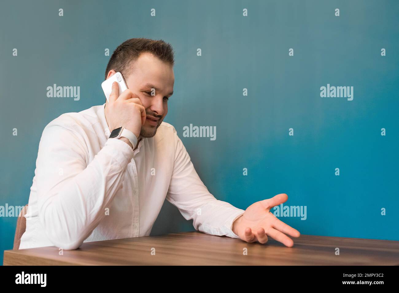 Cute businessman of European appearance with a beard and a white shirt talking on the phone sitting in a cafe and gesticulating with his hands. Stock Photo