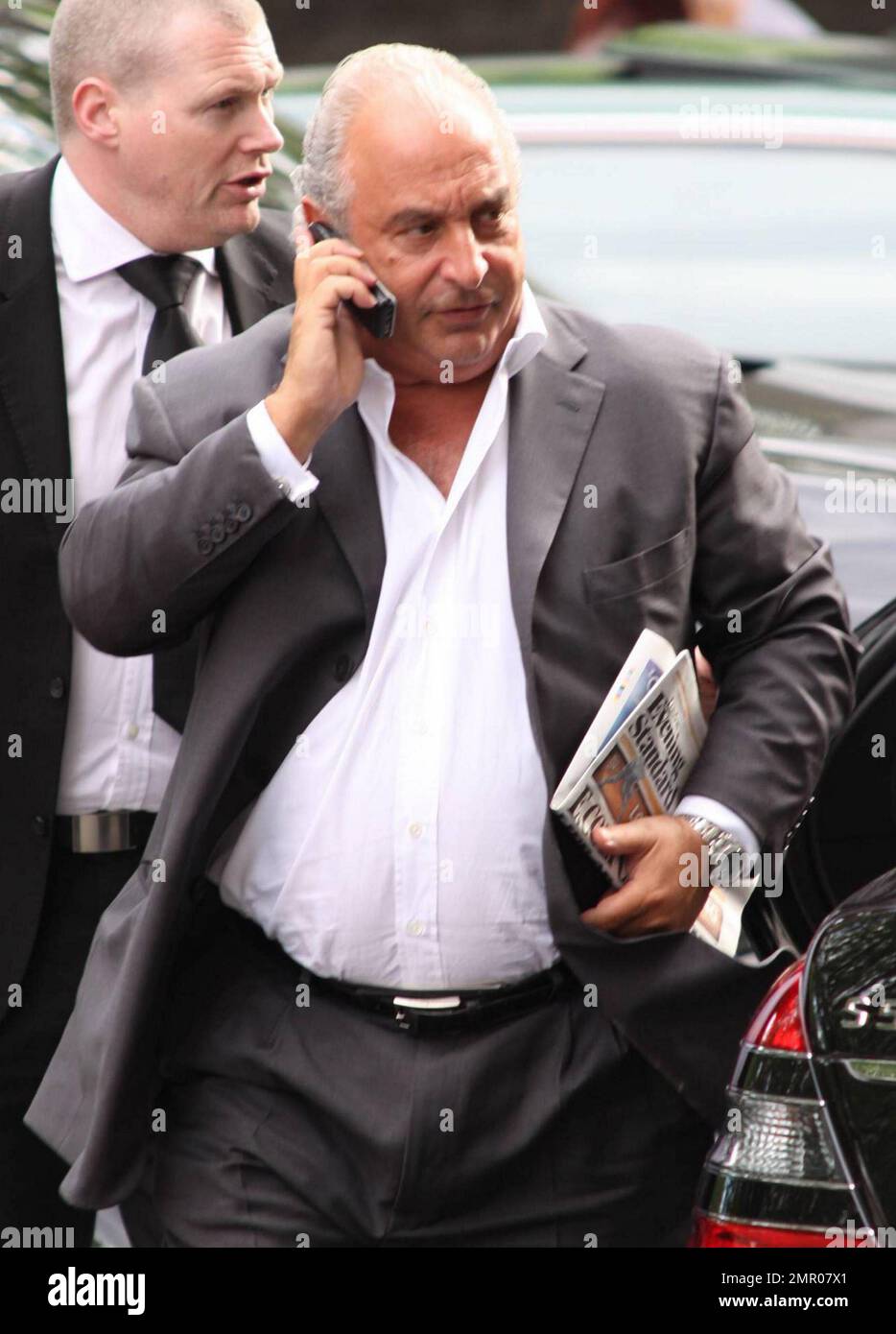 British billionaire businessman Sir Philip Green carries a newspaper and chats on his cell phone