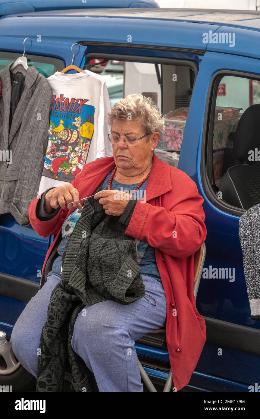 a woman is cutting the threads of a sweater with scissors while sitting on a seat in front of her car Stock Photo