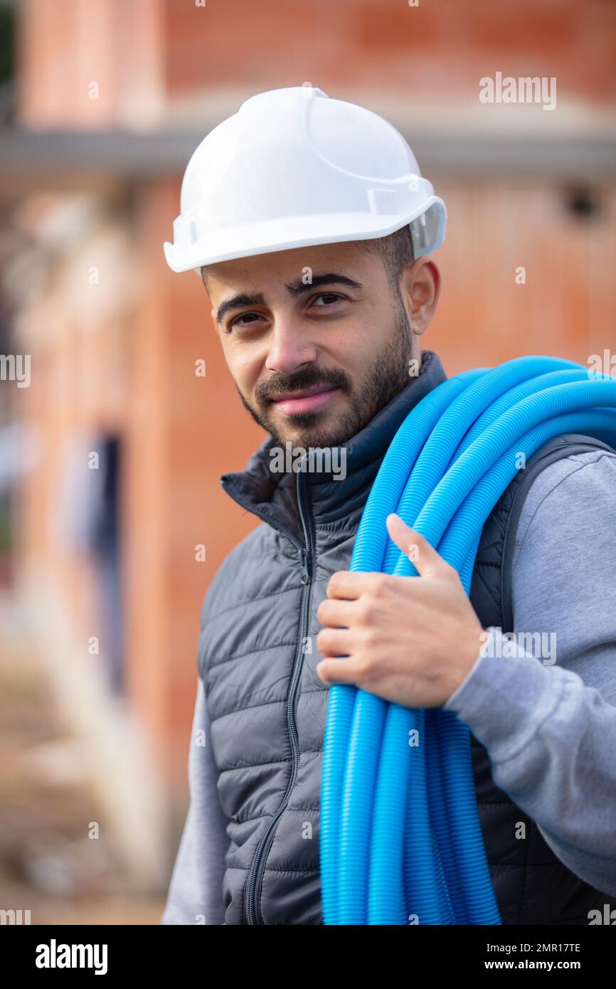 builder carrying a reel of blue pipe across his body Stock Photo
