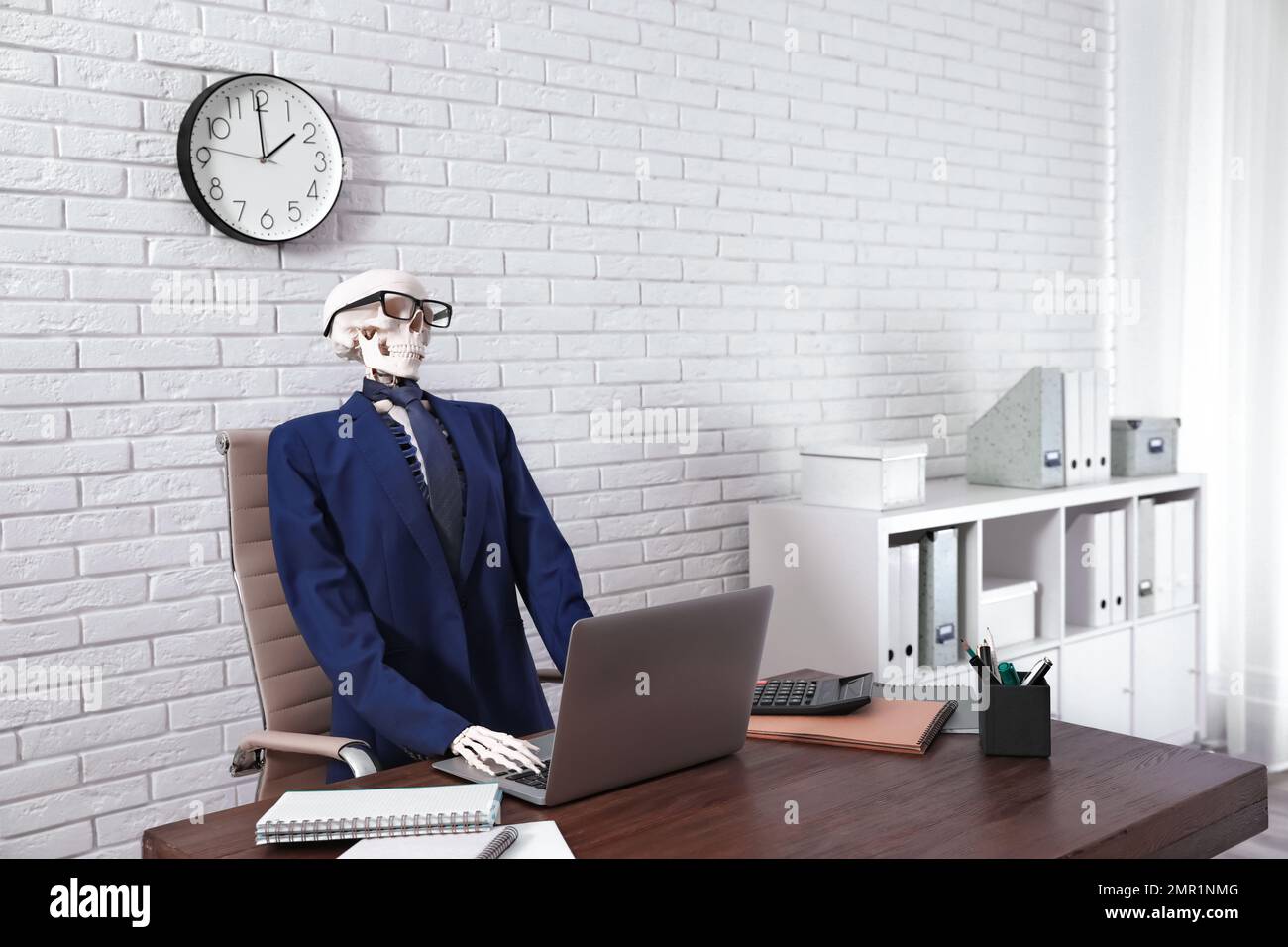 Human skeleton in suit using laptop at table in office Stock Photo