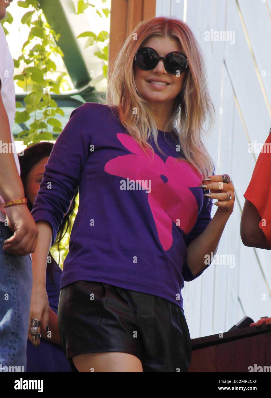 Wearing a purple sweater with a big pink flower design and black shorts, Fergie waves as she makes an appearance for an interview with Maria Menounos at Planet Dailies at The Grove shopping center. Los Angeles, CA. 16th October 2012. Stock Photo