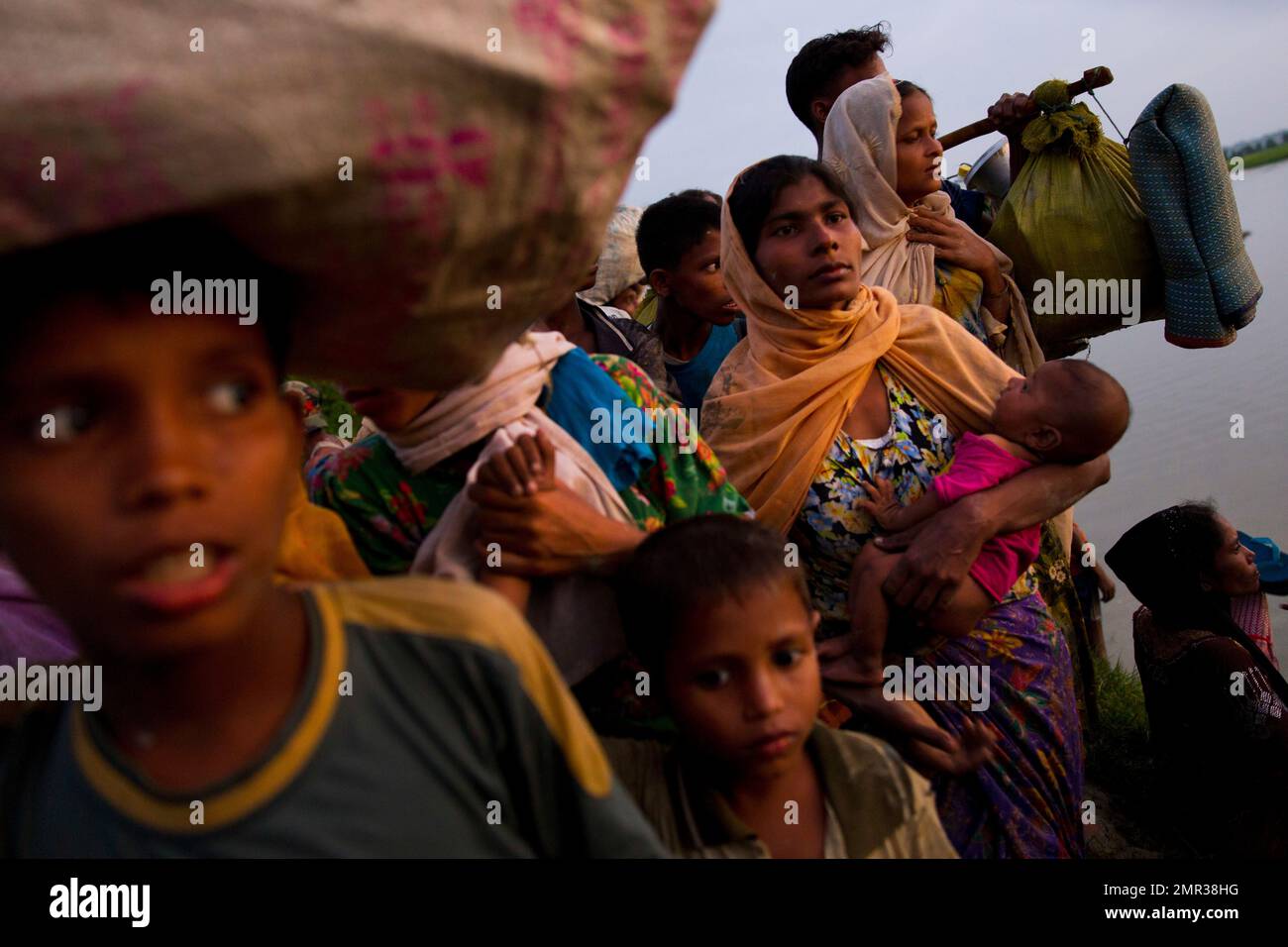 A Rohingya Muslim woman carries an infant child and walks with a group