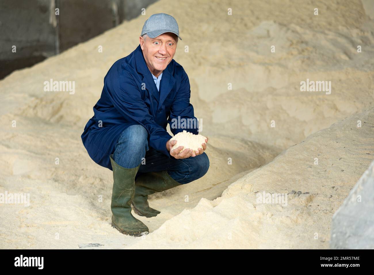 Happy dairy farm male worker holding corn flour animal feed for dairy cattle in farm storage area Stock Photo