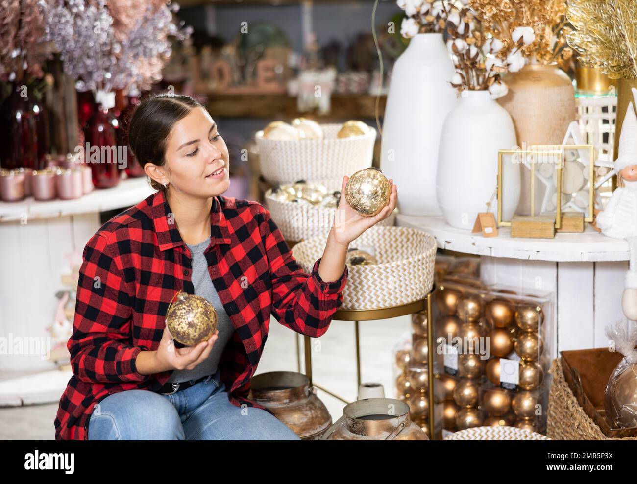 The excited young woman checking the material of Christmas bubbles while standing in a decorated hall Stock Photo