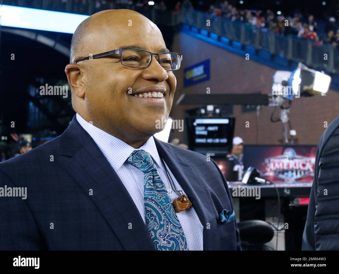 NFL sportscaster Mike Tirico stands on the sideline set before an NFL