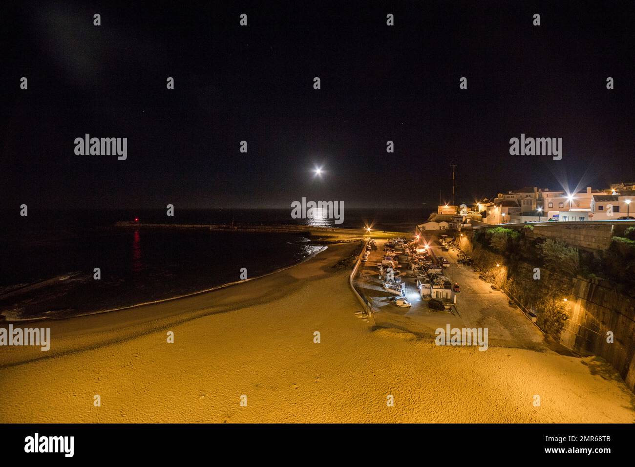 Moonset, pier and Praia dos Pescadores seen from Largo das Ribas, historic center of the village of Ericeira, on a winter night Portugal Stock Photo